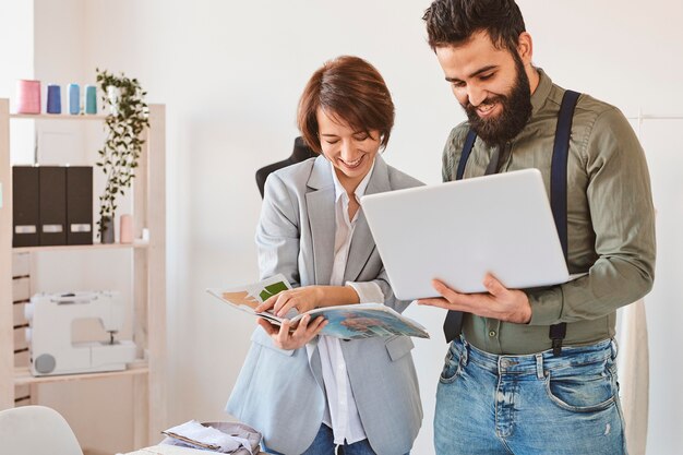 Designers de moda sorridente trabalhando em ateliê com laptop