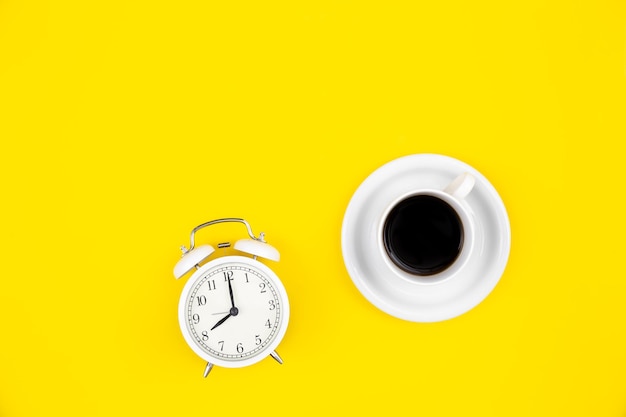 Despertador e uma xícara de café em uma vista superior de fundo amarelo