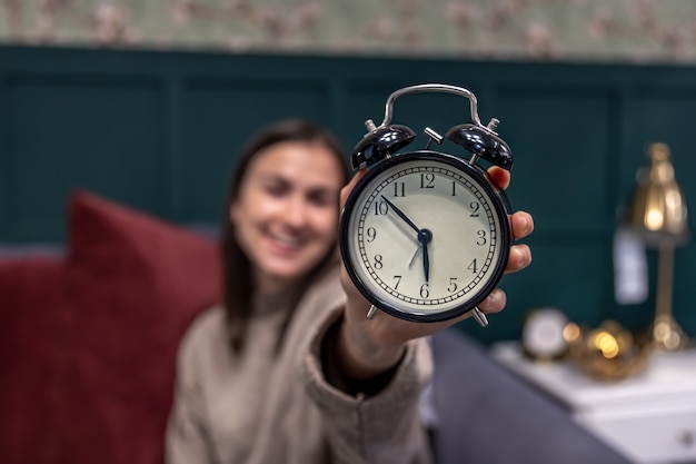 Despertador retro vintage preto nas mãos femininas em um fundo desfocado.