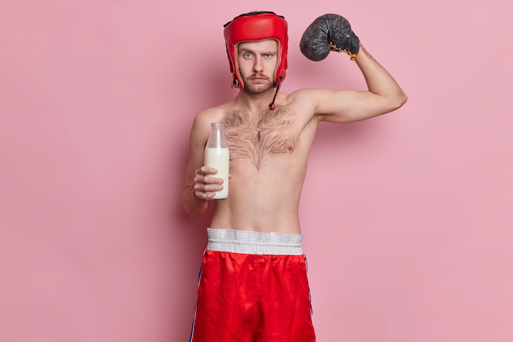 Foto grátis desportista autoconfiante sério levanta o braço mostra seus músculos fortes bebe leite mantém a dieta de proteínas usa chapéu e bermuda fica com o torso nu