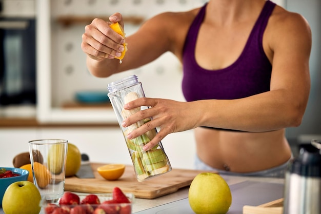 Desportista irreconhecível usando limão enquanto faz smoothie de frutas em casa