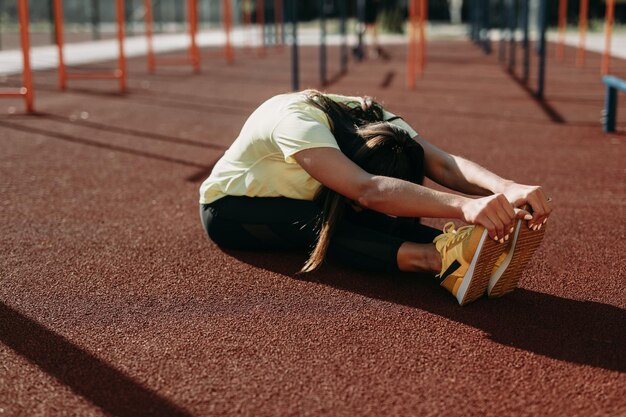 Desportiva jovem morena esticando os músculos após o treino