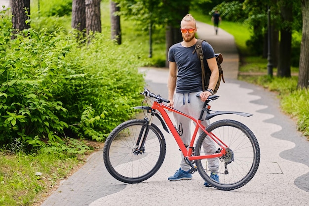 Desportivo macho barbudo senta-se em uma bicicleta de montanha vermelha ao ar livre.