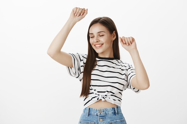 Despreocupada garota atraente festeira dançando de olhos fechados, olhos fechados, sorriso satisfeito