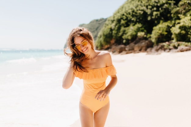 Despreocupada senhora caucasiana, posando com prazer na praia. modelo muito feminino com pele bronzeada, caminhando na praia.