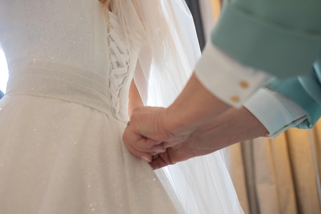 Detalhe das mãos das damas de honra puxando a fita sating do espartilho do vestido de noiva das noivas durante o vestir