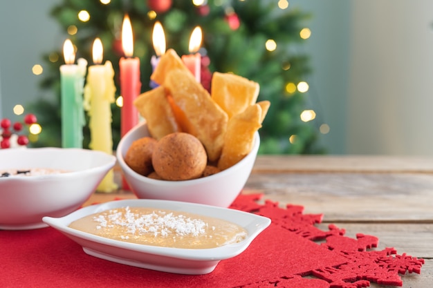 Dia da luz de velas. comida típica colombiana. buñuelo, creme e flocos com velas e árvore de natal ao fundo. feriado colombiano tradicional.