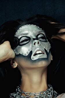Dia das bruxas, feriados, estilo de vida, pessoas, beleza, conceito criativo - tema de halloween e maquiagem criativa: modelo de menina bonita com corpo preto com máscara prateada pintura do crânio em fundo escuro no estúdio