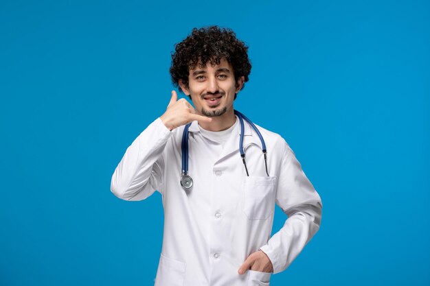 Dia dos médicos cara bonito e bonito em uniforme médico fazendo gesto de telefonema