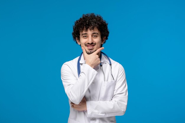 Dia dos médicos cara bonito e bonito em uniforme médico pensando alegremente