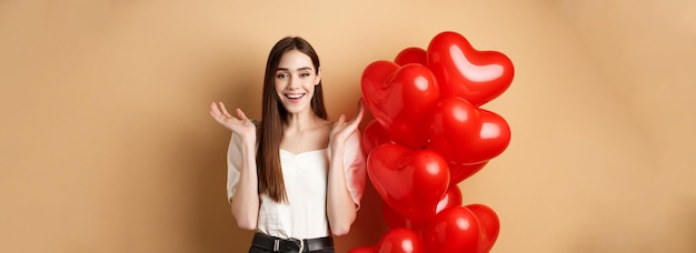 Foto grátis dia dos namorados e conceito de amor feliz mulher sorridente levantando as mãos surpresa em pé perto de romanti