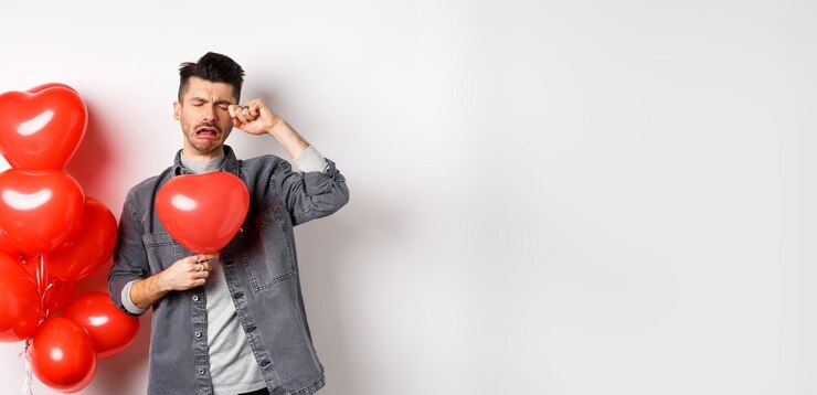 Foto grátis dia dos namorados e conceito de amor triste homem chorando segurando balão de coração vermelho e lágrimas em pé