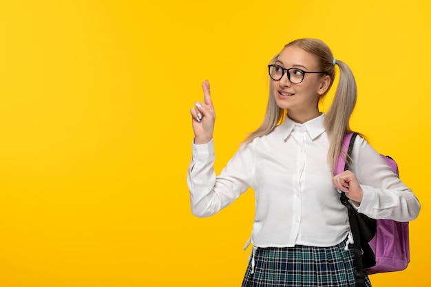 Dia mundial do livro, uma estudante feliz e bonita cruzou os dedos em fundo amarelo uniforme