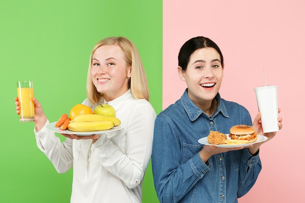 Dieta. Conceito de dieta. Comida saudável. Moças lindas escolhendo entre frutas e fast food deselegante