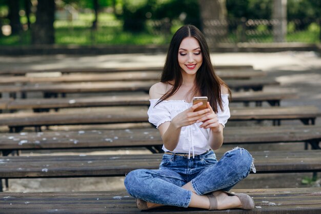 digitando Menina bonita em seu telefone sentado no banco em um parque