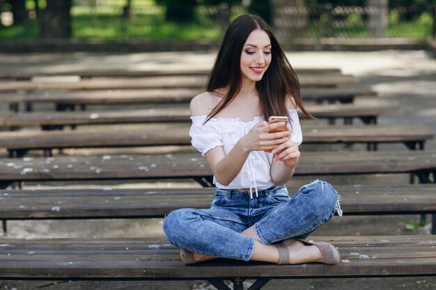 digitando Menina bonita em seu telefone sentado no banco em um parque