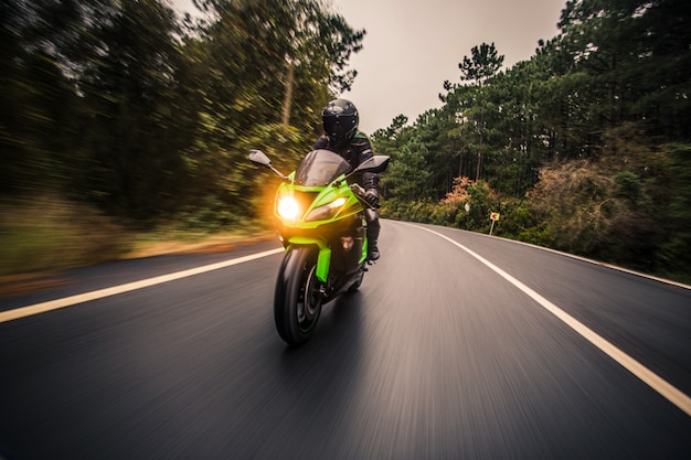 Dirigindo a motocicleta de cor verde neon na estrada na hora do crepúsculo.