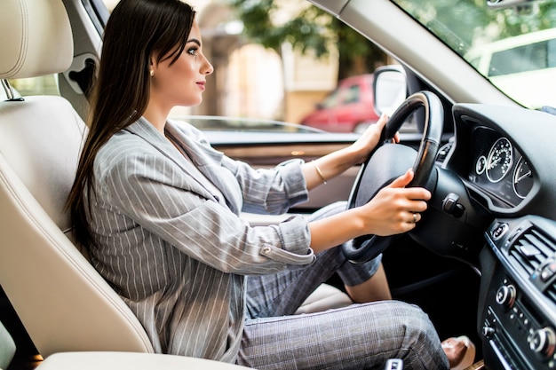 Dirigindo pela cidade. Mulher jovem e atraente sorrindo e olhando diretamente enquanto dirige um carro