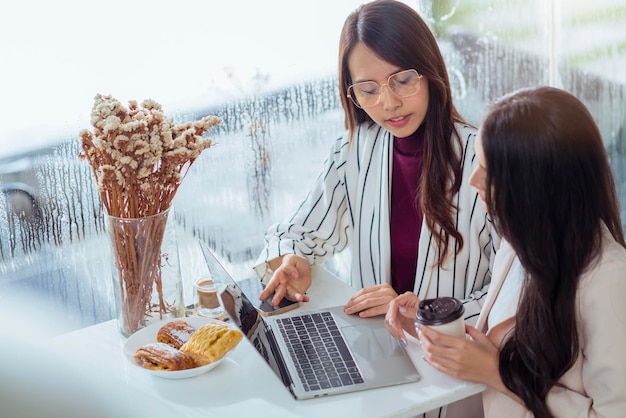 Discussão de reunião casual de agência criativa feminina asiática trabalhando com café de laptop trabalhando em casa com colega de trabalho jovem mulher asiática com janela e chuva de água chovendo fundo