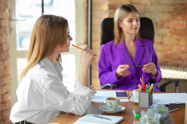 Discussão. Mulher de negócios caucasiana jovem em um escritório moderno com a equipe. Reunião, entrega de tarefas. Mulheres trabalhando no escritório. Conceito de finanças, negócios, poder feminino, inclusão, diversidade, feminismo.