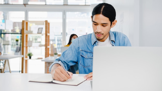 Distanciamento social do empresário Ásia na nova situação normal para prevenção de vírus usando laptop apresentação para colega sobre o plano de videochamada enquanto trabalha no escritório em casa. Estilo de vida após o vírus corona.