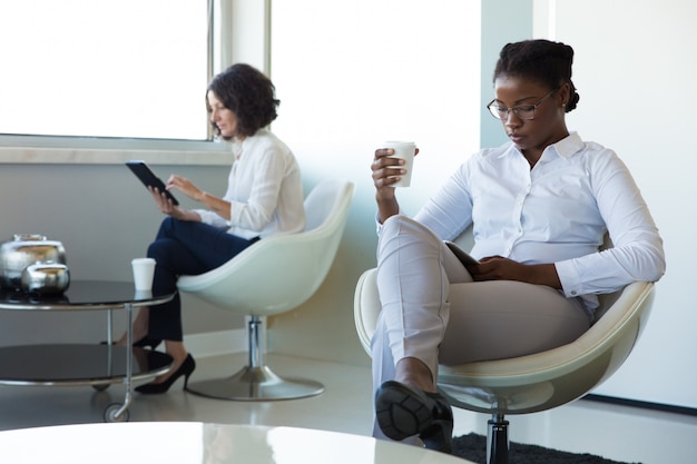 Diversas mulheres de negócios com gadgets bebendo café