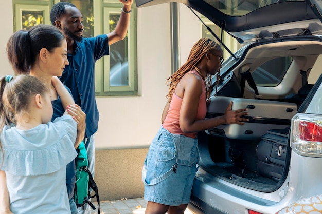 Diversos familiares e amigos saindo em viagem, carregando sacos infláveis e carrinhos no porta-malas do veículo para viajar nas férias de verão. Indo para o destino à beira-mar com pessoas sorridentes.