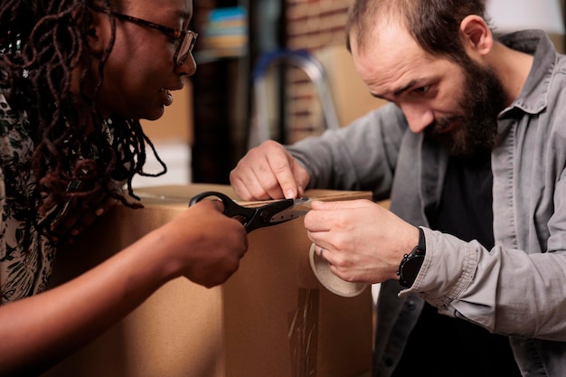 Diversos parceiros de vida usando fita adesiva e tesoura para embalar móveis em caixas, movendo-se juntos em novas propriedades domésticas. embalando coisas com rolo adesivo para mover em apartamento alugado. fechar-se.