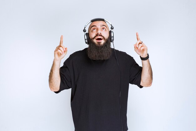 DJ com barba usando fones de ouvido e apontando para cima.