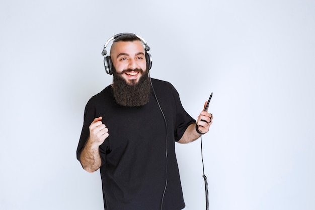 Dj com barba usando fones de ouvido e curtindo a lista de reprodução em seu telefone.