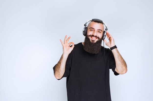 DJ com barba usando fones de ouvido e mostrando sinal positivo com a mão.