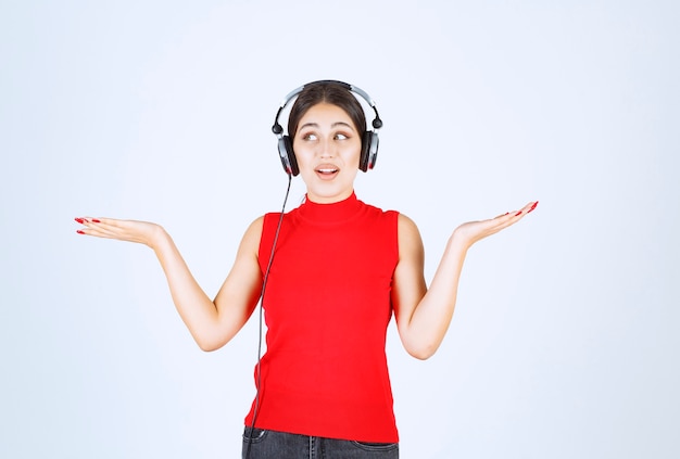 Dj garota de camisa vermelha com fones de ouvido apontando algo ou mostrando algo na mão.