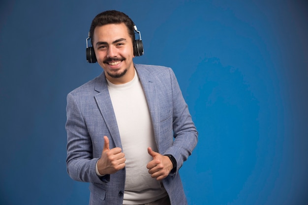 DJ masculino em terno cinza usando fones de ouvido e dançando.