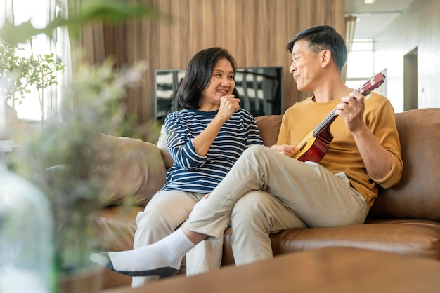 Doce casal asiático sênior canta tocando instrumento de ukulele acústico Feliz sorrindo Avós idosos se divertindo e curtindo sua vida de aposentadoria Estilo de vida Festa estilo de vida feliz
