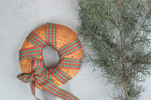 Doce e deliciosa rosquinha amarrada em um laço festivo no ramo da árvore de natal