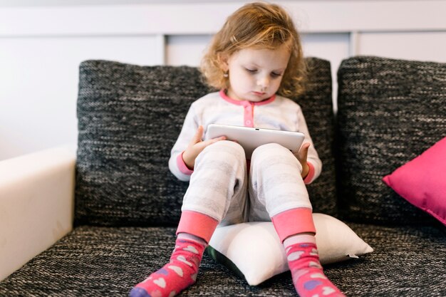 Doce menina com tablet no sofá