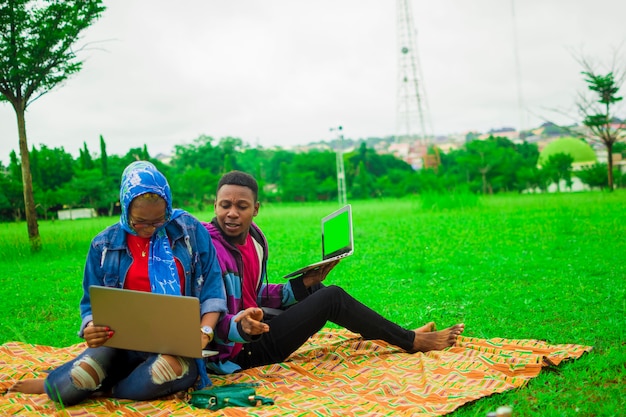 Dois africanos felizes se divertindo ao ar livre com um laptop - conceito de amizade com um menino e uma menina nas férias de primavera - melhor estilo de vida moderno