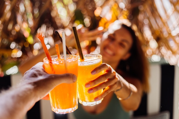 Dois amigos a tilintar em copos de saborosos cocktails tropicais num dia de sol num café