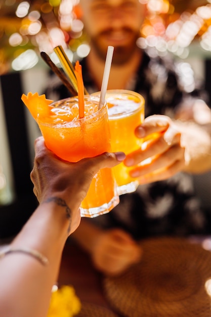 Dois amigos a tilintar em copos de saborosos cocktails tropicais num dia de sol num café