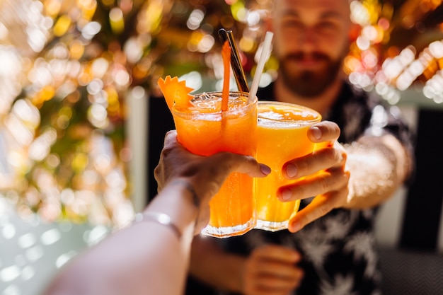 Dois amigos a tilintar em copos de saborosos cocktails tropicais num dia de sol num café