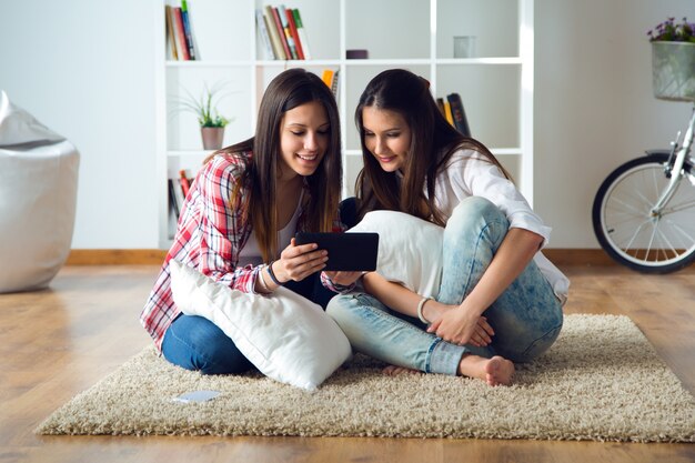 Dois amigos bonitos da mulher nova que usam a tabuleta digital em casa.