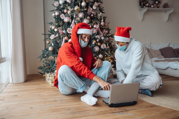 Dois amigos com chapéu de Papai Noel perto do laptop estão interagindo por meio de videochamadas. Natal isolado em casa. Distanciamento social para férias.