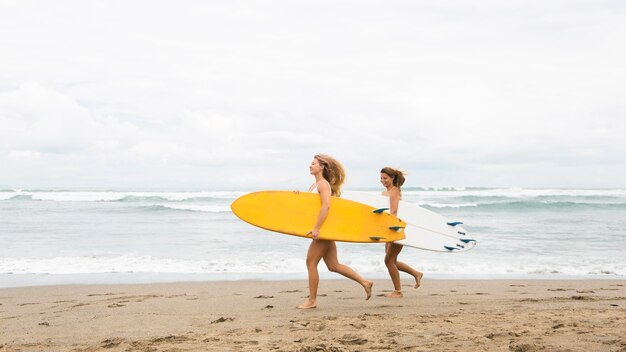 Dois amigos sorridentes correndo na praia com pranchas de surfe e cópia de espaço