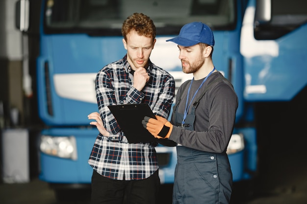 Dois caras conversando sobre trabalho. Trabalho na garagem perto do caminhão. Transferência de documentos com mercadorias