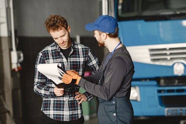 Dois caras conversando sobre trabalho. Trabalho na garagem perto do caminhão. Transferência de documentos com mercadorias