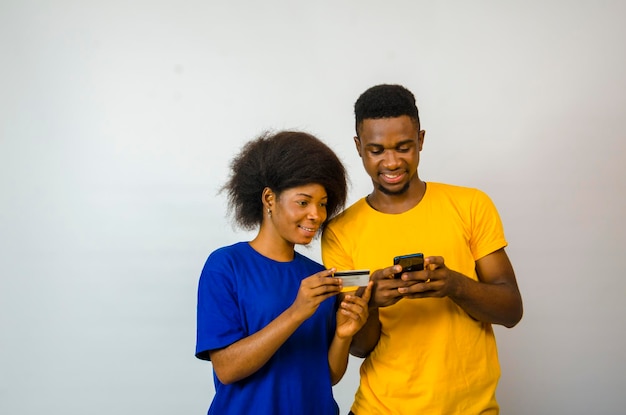Dois casais africanos bonitos isolados sobre fundo branco usando seu celular e cartão de crédito para fazer compras online