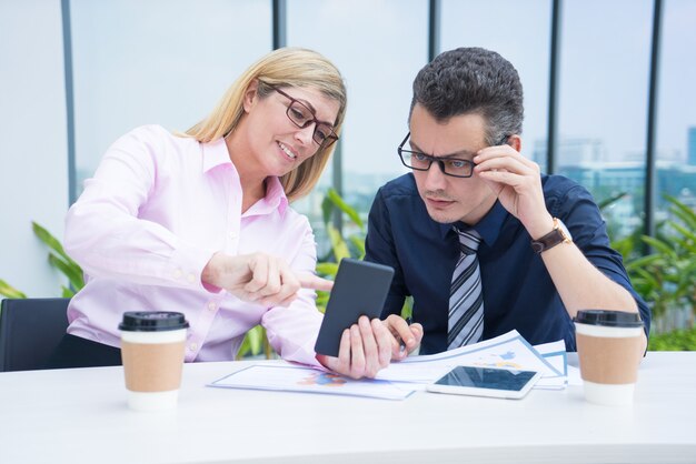 Dois colegas adultos meados de do negócio que usam o telefone no café ao ar livre.