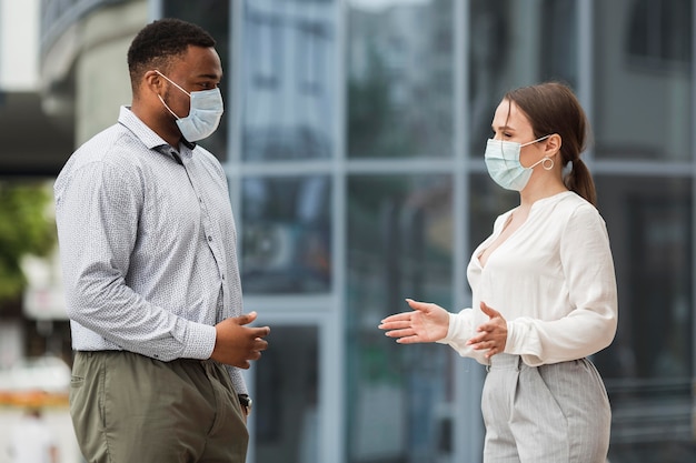 Dois colegas conversando ao ar livre durante a pandemia com máscaras