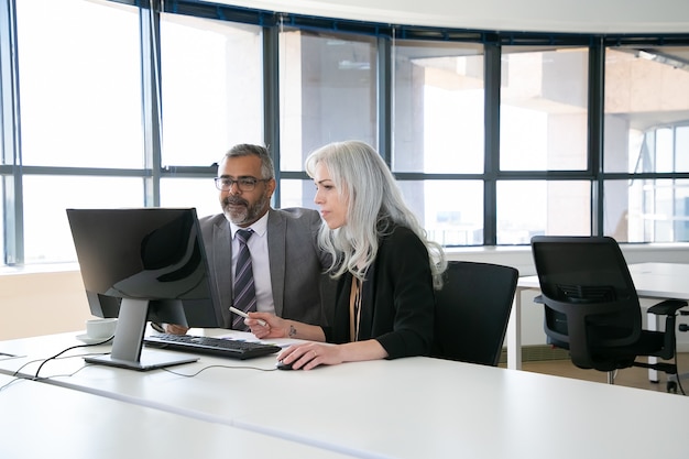 Dois colegas de trabalho concentrados assistindo conteúdo no monitor do computador, segurando a caneta e o mouse. Comunicação empresarial e conceito de trabalho em equipe