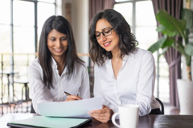 Dois colegas de trabalho fêmeas de sorriso que planeiam no café.